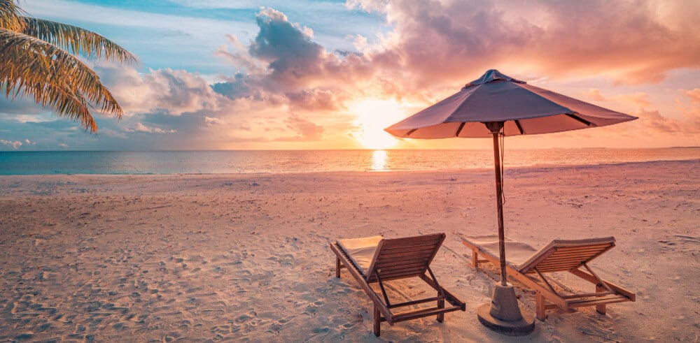 Hermosa puesta de sol tropical pareja tumbonas paraguas bajo palmera paisaje romántico de vacaciones